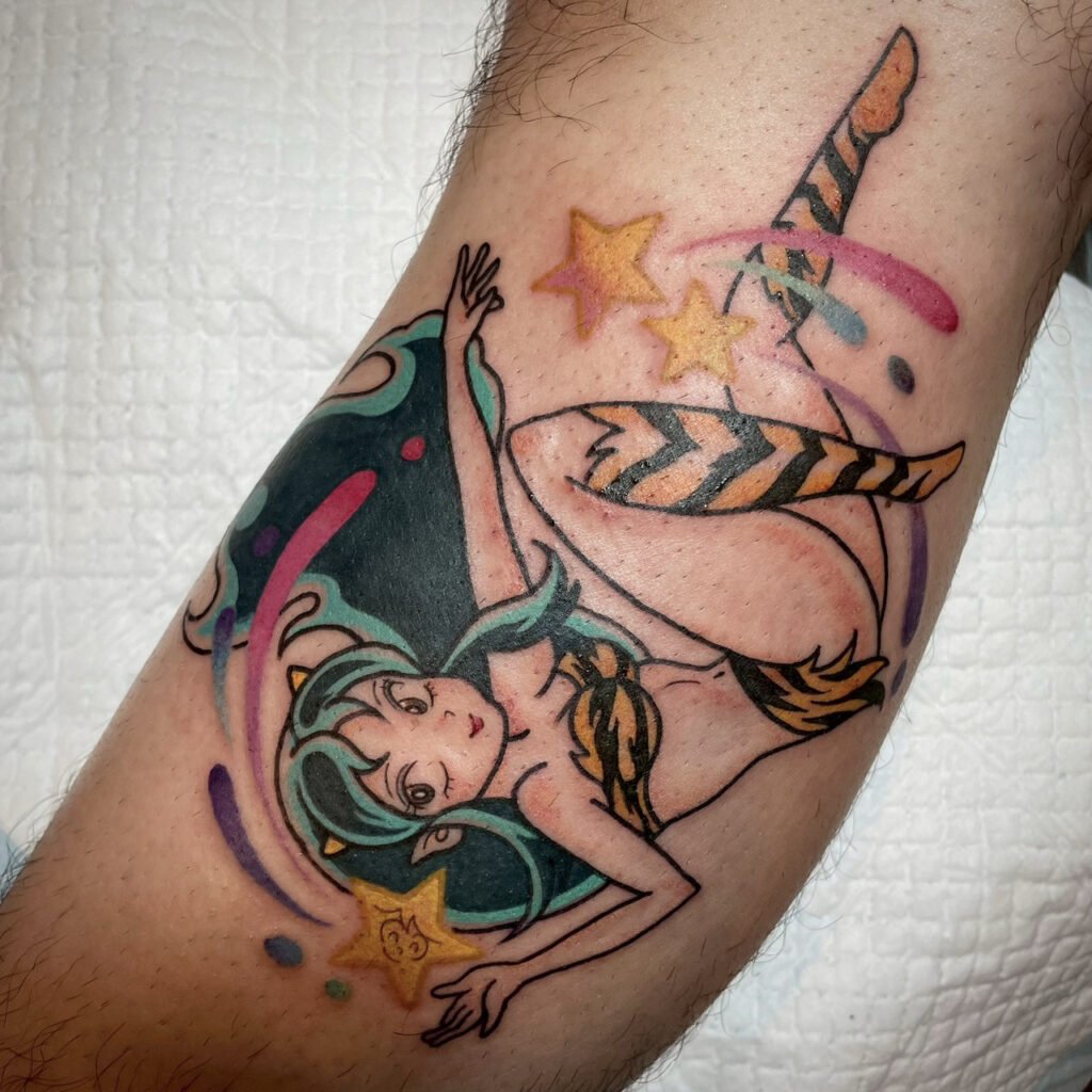 Color tattoo of Lum from Urusei Yatsura in a dynamic floating pose, featuring her iconic tiger-stripe outfit, green hair, and bright star accents with colorful motion strokes.