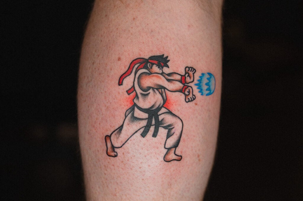 American Traditional–style Ryu tattoo launching a Hadouken with bold lines and simple colors.