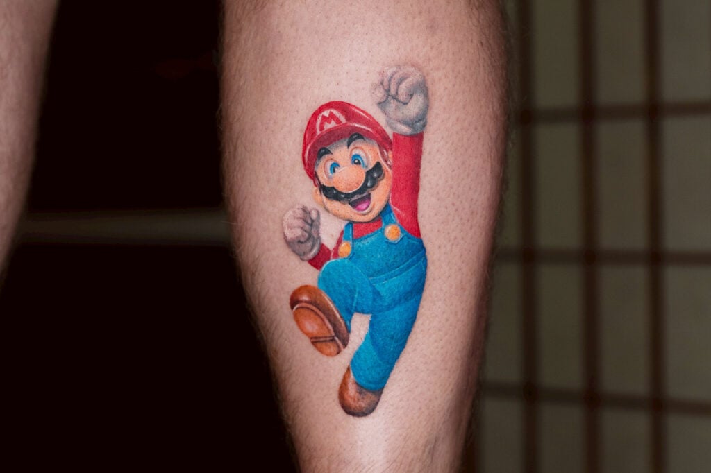 Realistic 3D-style Mario tattoo with bright colors and glossy white highlights, created at Good Times Ink Osaka.