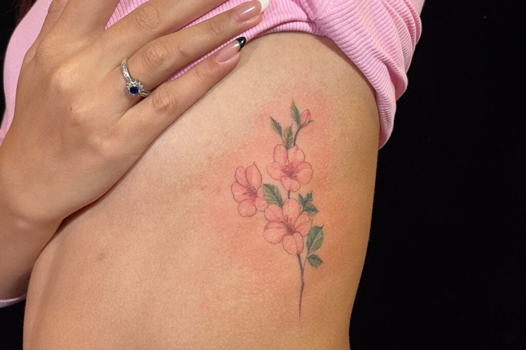 Light watercolor-style sakura tattoo with soft pink petals, created at Good Times Ink Osaka.