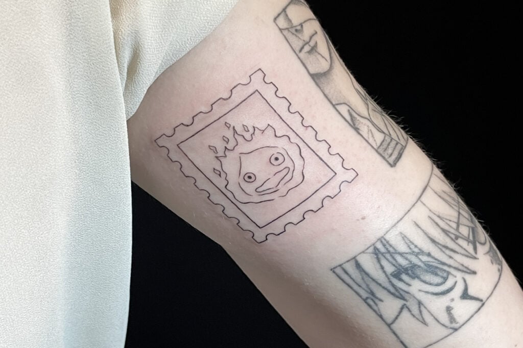 Calcifer postage‑stamp styled tattoo, small collectible format, Osaka.