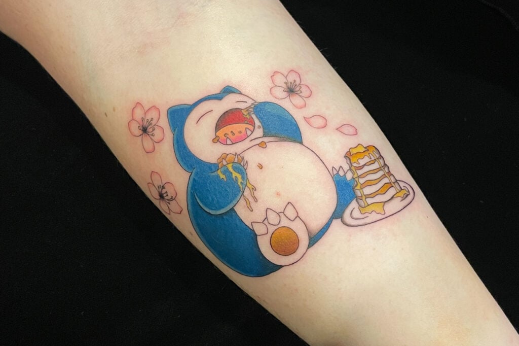Snorlax tattoo eating pancakes with sakura petals for a Japanese touch, created at Good Times Ink Osaka.
