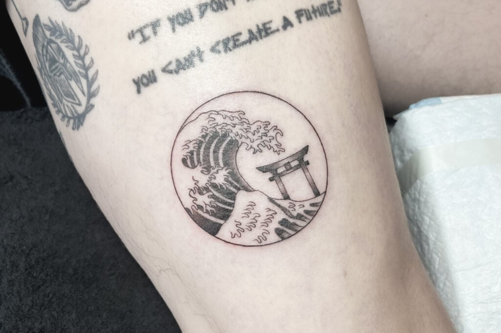 Fine-line Hokusai wave tattoo with torii gate inside a circle, created at Good Times Ink Osaka.