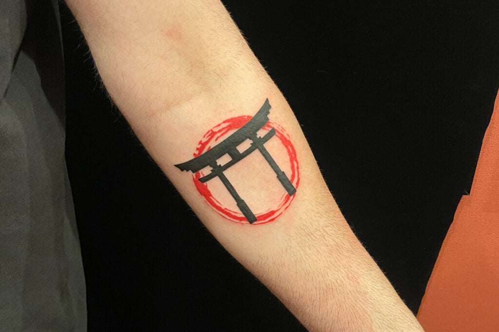 Torii gate tattoo inside a red brush circle, created at Good Times Ink Osaka.