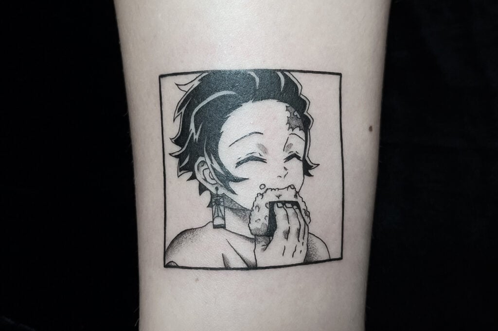 Tanjiro eating an onigiri in a soft, cheerful manga-panel style tattoo, captured in a simple boxed frame.