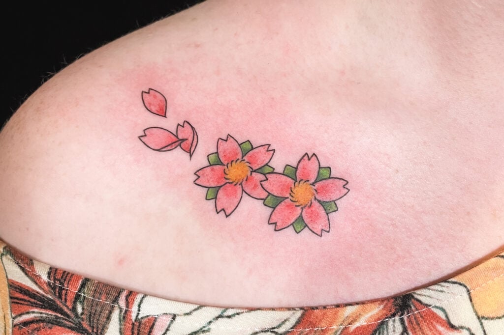 Small sakura flower tattoo with drifting petals in color, created at Good Times Ink Osaka.