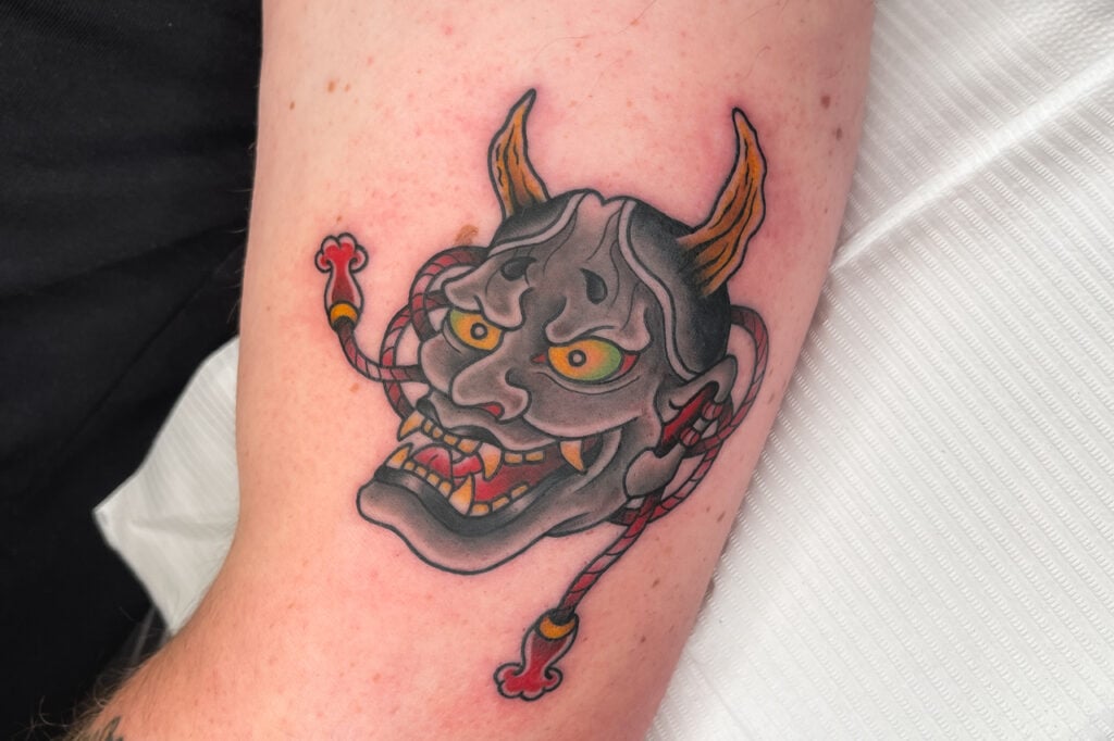 Small black-and-gray Hannya mask tattoo, created at Good Times Ink Osaka.