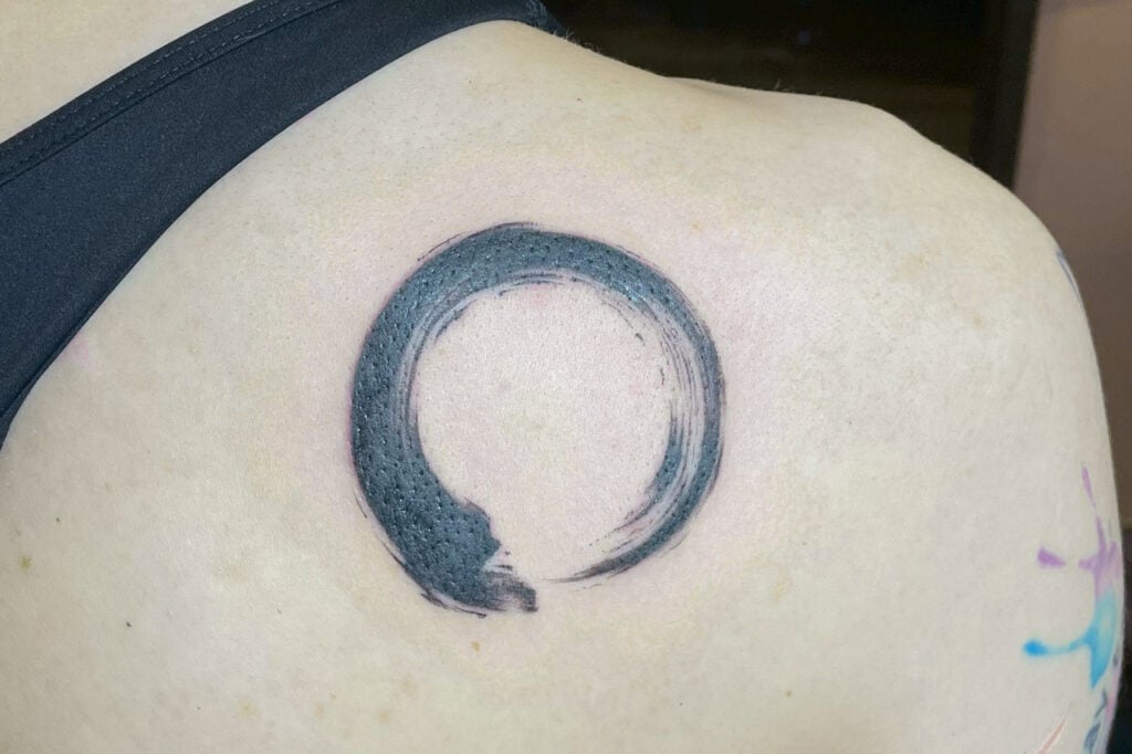 Simple brush-stroke enso tattoo in black ink, created at Good Times Ink Osaka.